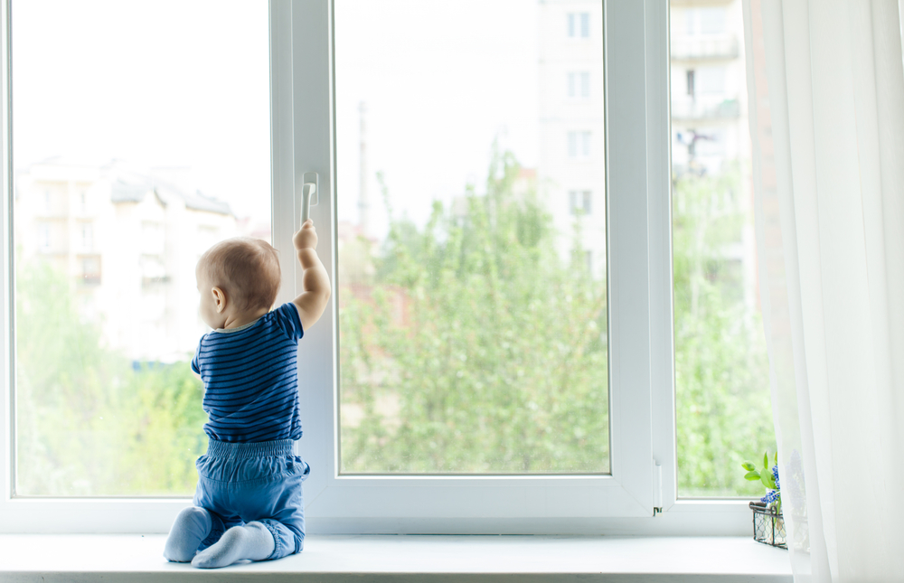 A baby standing beside a window
